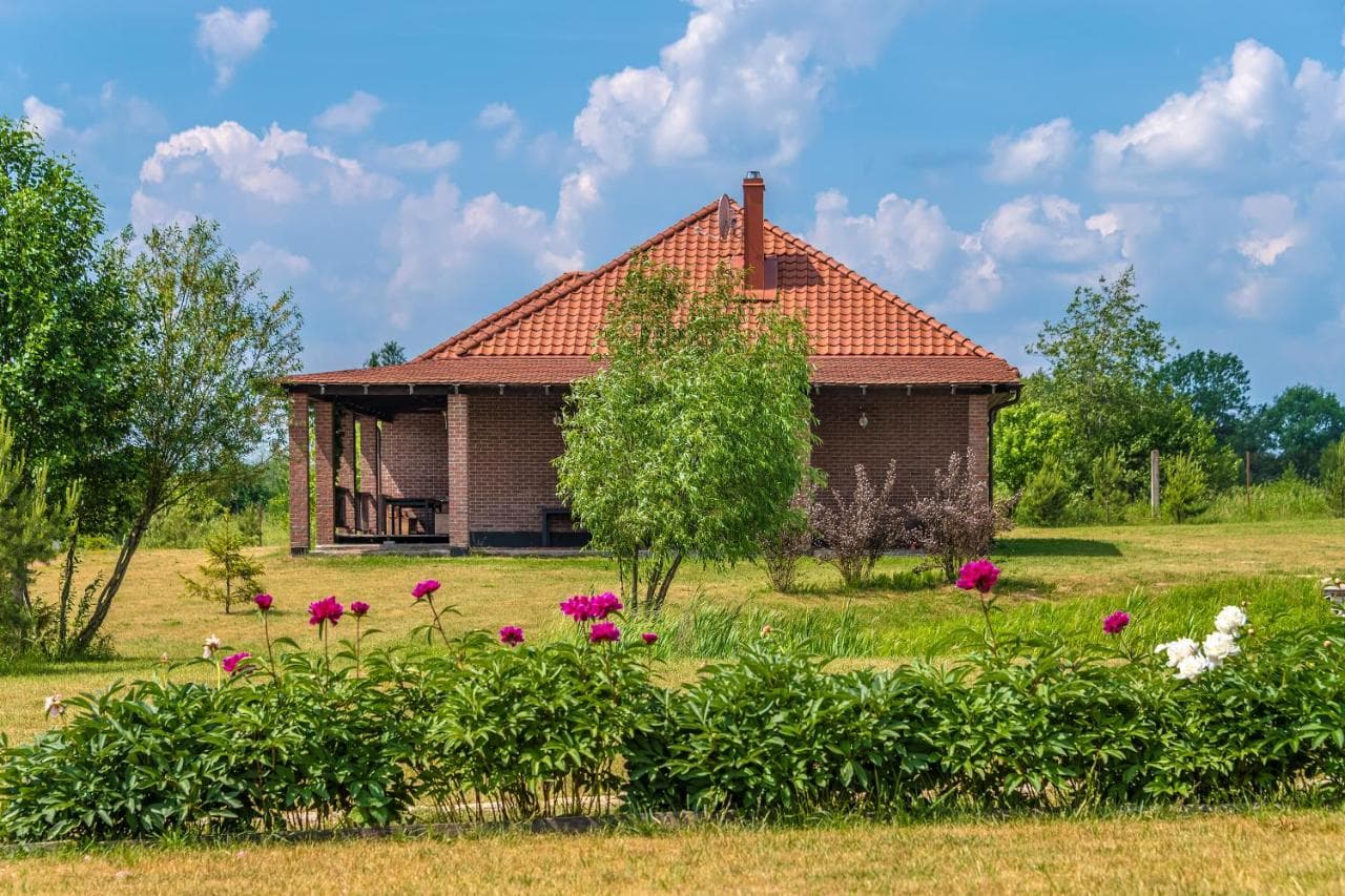 Svečių namas su čerpių stogu, gėlių vazonais ir žydintis pieva