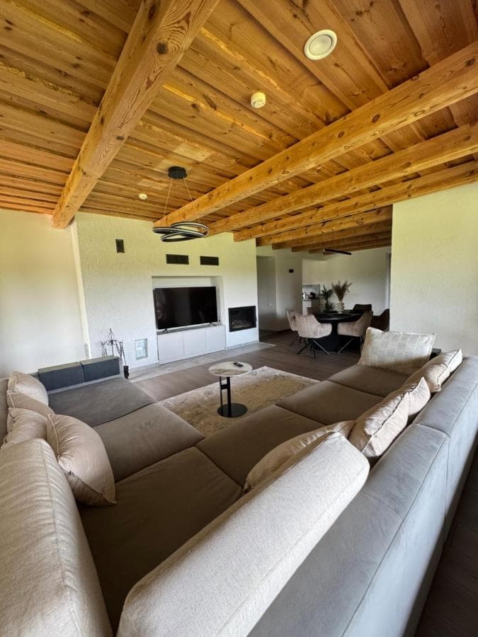 Moderni svetainė su didžiule sekcijine sofa, televizoriumi ir židiniu po mediniu lubomis